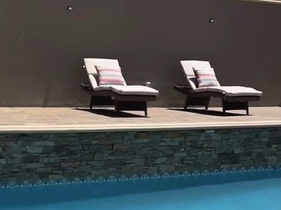 Lounge chairs on the paver pool deck beside a stone-faced pool wall in La Verne, CA